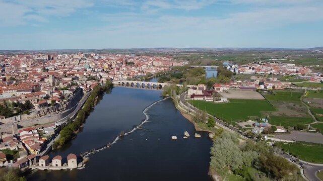 4K high-altitude aerial drone video flying over the city of Zamora, Spain, located on the banks of the Duero River. The panoramic shot features the historic city center, the green natural park on the