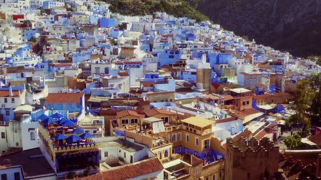 Drone rises over Chefchaouen medina to top-down view, revealing blue rooftops and winding streets.