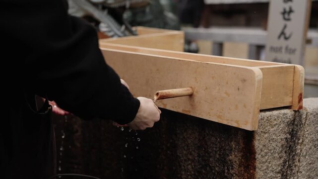 Person rinsing hand under flowing water from bamboo spout of wooden temizuya purification basin at a Shinto shrine