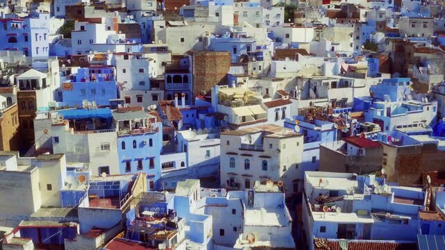 Drone descends close over Chefchaouen medina, revealing dense blue and white rooftop architecture.