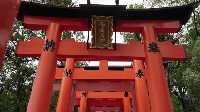 Looking up through layered red torii gates with gold Inari Okami plaque and kanji at Fushimi Inari Kyoto