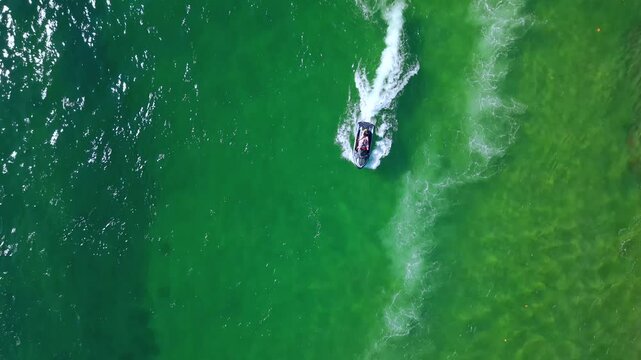 Overhead drone shot of a jet ski wave runner speeding across vivid green blue turquoise ocean water seen from directly above on a clear sunny day
