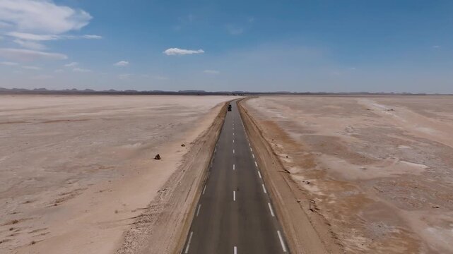 Aerial view of the empty asphalt highway stretching infinitely across the dry Chott el Djerid salt lake. Overland adventure travel and infrastructure in the Tunisian desert