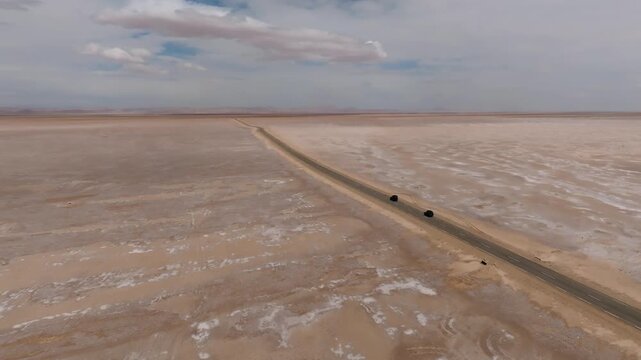Aerial drone shot of off-road vehicles driving on the long asphalt road across Chott el Djerid salt lake. Crystalline salt flats and vast desert horizon in southern Tunisia