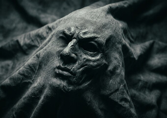 Fototapeta premium A dark grey fabric or stone sculpture forms a dramatic face with an angry expression and deep wrinkles that blend into the surrounding folds of cloth