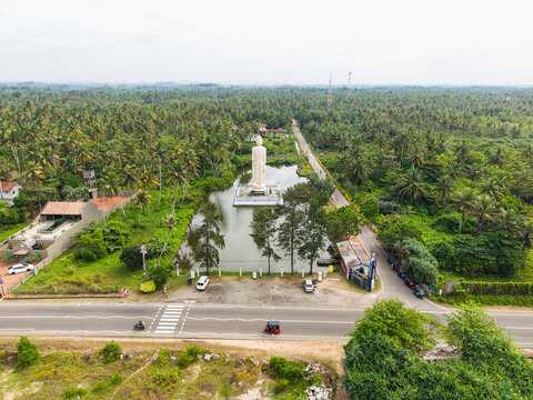 Aerial view of the Tsunami Honganji Viharaya standing Buddha statue surrounded by a pond and lush palm trees Peraliya, Southern Province, Sri Lanka.
