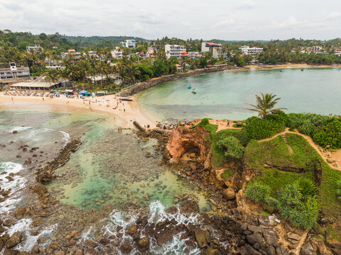 Aerial view of Parrot Rock and the sandy beach with turquoise water and lush palm trees in Mirissa, Southern Province, Sri Lanka.