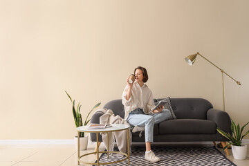 Young pretty woman using tablet and drinking coffee on sofa in light living room