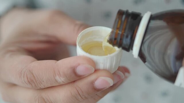 Pouring liquid medicine from a bottle into a cap