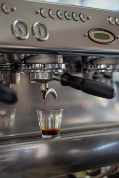 Espresso extraction from espresso machine into glass cup close-up.