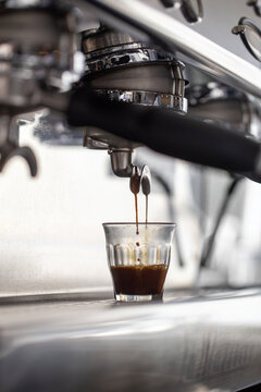 Low angle view of rich espresso pouring into clear glass cup.