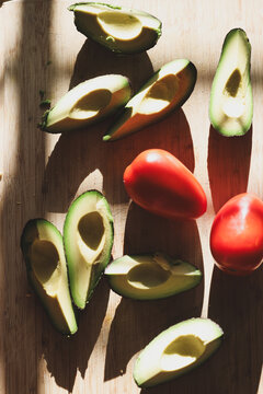 Fresh green avocado sliced and ready to eat along with whole organic roma tomatoes on a cutting board. Delicious healthy, nutritious food.