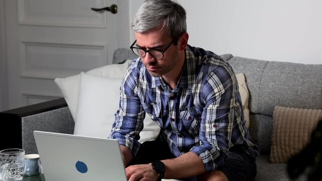 Man works on laptop at home office while managing remote tasks and staying productive in a modern workspace setup