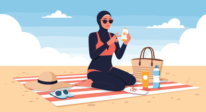 Muslim woman wearing a modest burkini sitting on a beach towel and applying sunscreen from a tube on a sunny day.
