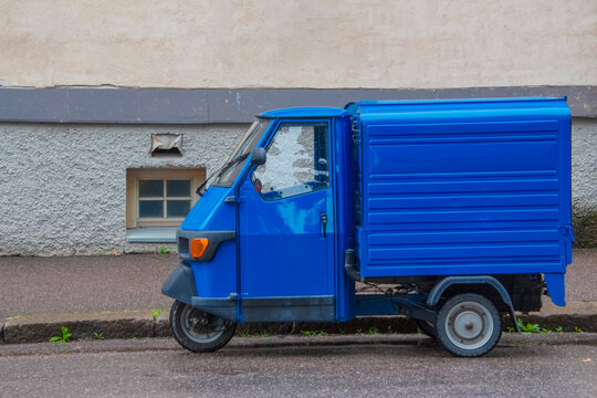 Blue three-wheeled postal vehicle with a van parked on the street