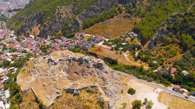 Fethiye, Turkey. Aerial drone view of Fethiye Castle ruins with large Turkish flag on flagpole on the hilltop, overlooking the city and ancient Lycian rock tombs in the cliffs on a sunny day.