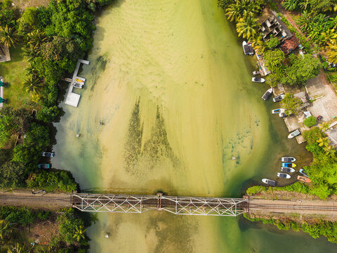 Aerial view of Koggala Lake with a railway bridge crossing the water, moored boats, and lush tropical vegetation in Koggala, Southern Province, Sri Lanka.