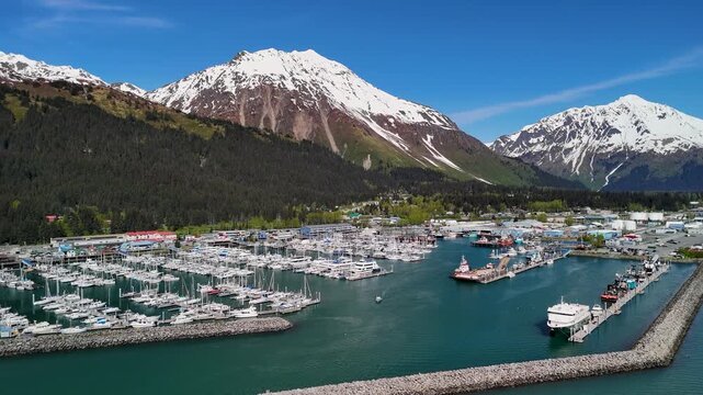 Seward, Alaska downtown sits near the shoreline bay area under a clear blue sky in summer. Boats, buildings, and mountains create a scenic coastal view. Perfect stock footage for travel, tourism, city