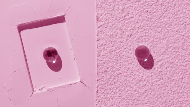 Overhead perspective shot of a light pink half flattened, half sifted powder surface with a rectangle imprint and two hydrogel spheres on top, illuminated by orbiting light creating shadow movement