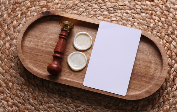 White business card and Vintage sealing wax stamp in wooden tray on woven straw mat.