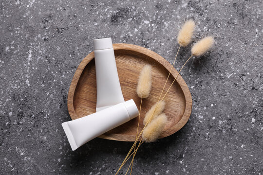 White blank cream tubes in wooden tray on concrete background with dry grass. Beauty concept