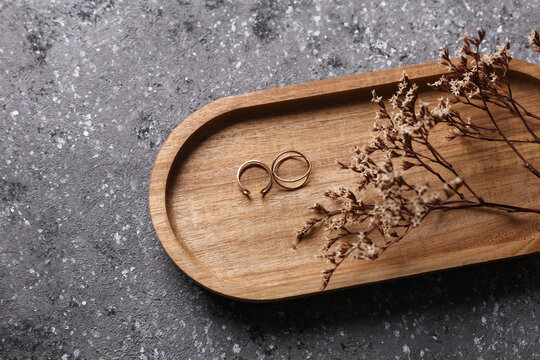 Gold rings in a wooden tray on dark concrete background with dry grass