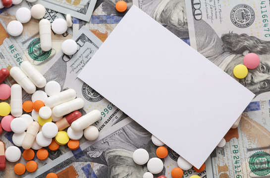 White blank business card and Many different pills on hundred dollar bills. Medicine financing concept
