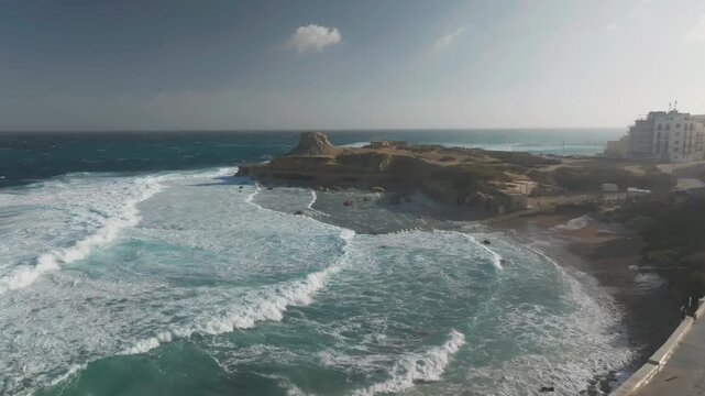 Rocky Coastline With Distinct Hillock Il-Qolla l-Bajda On Xwejni Bay In Gozo, Malta. aerial pullback shot