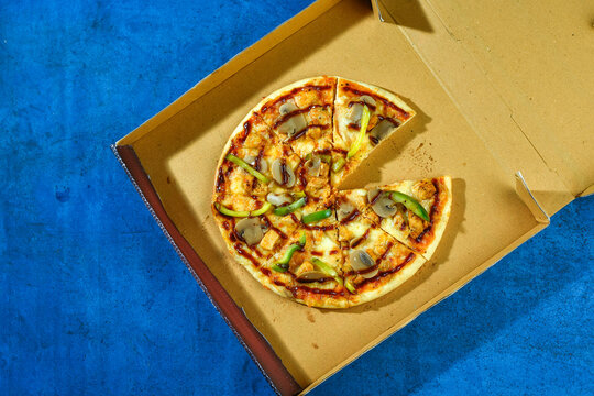 A delicious pizza with various toppings served in an open cardboard box on a blue surface
