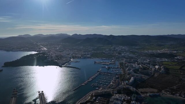 Right side ccokpit window spinning view of Ibiza city (IBZ)), harbor and surroundigs in a bright afternoon, with a radiant sun illuminatiing the Mediterranean Sea. 4K shot