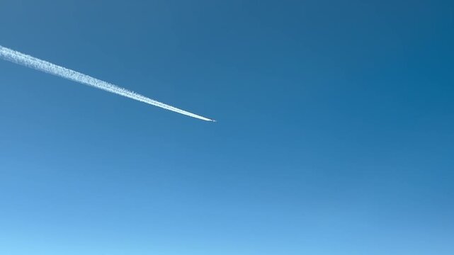 Cockpit view at cruise of a jet airplane and its fading contrail in a blue sky, diagonal crossing.