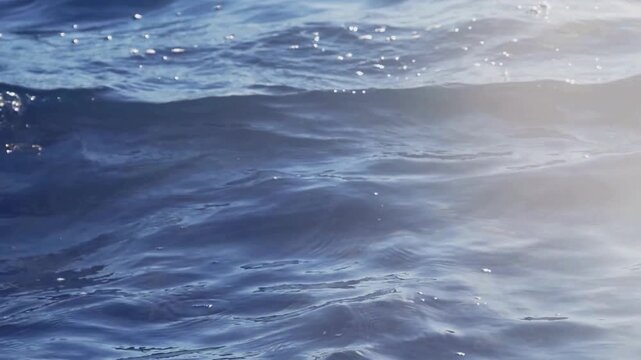 Blue ocean water ripples with sunlit highlights and bright reflections, creating sparkles and rhythmic gentle motion, perfect for relaxationthemed projects.