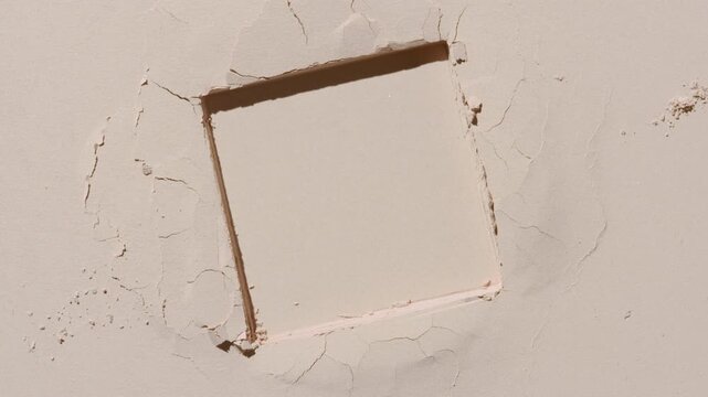 Overhead perspective shot of a beige flat powder surface with a stamped square mark illuminated by orbiting directional light creating shadow movement