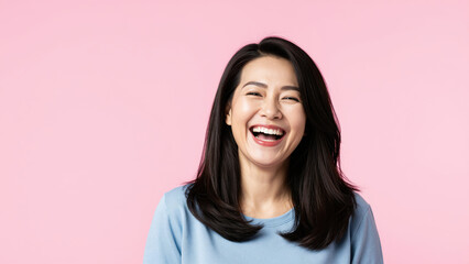Joyful Laughter: A radiant Asian woman with a warm smile bursts into hearty laughter, her eyes sparkling with mirth against a soft pink backdrop.