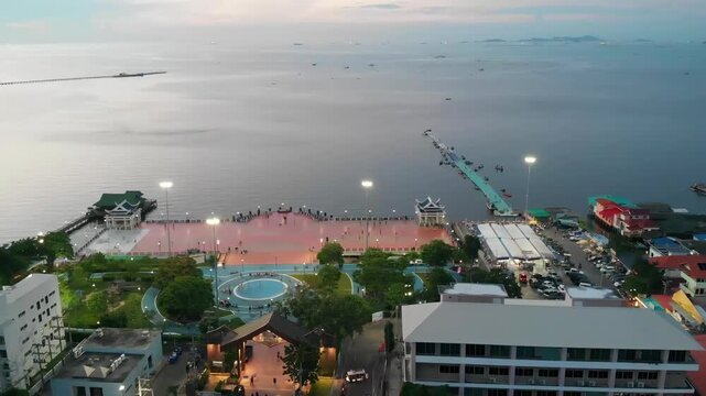 Pattaya Bali Hai Pier and Coastal City Skyline Landscape at Dusk - Standard Color. Wide backward aerial drone shot revealing the vibrant public plaza, public park, and long pier bridges next to the tw