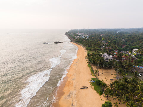 Aerial view of a sandy beach coastline with ocean waves crashing on the shore and palm trees lining the coast in Galle, Southern Province, Sri Lanka.