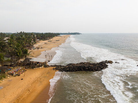 Aerial view of golden sandy beach with palm trees, a small beach bar, and a rock breakwater along the coastline in Galle, Southern Province, Sri Lanka.