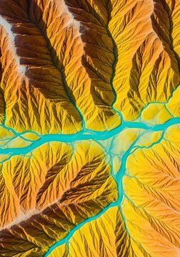 Vibrant yellow and orange earth features intricate teal streams branching out in an abstract aerial pattern across the rugged landscape, liquid, water, stream