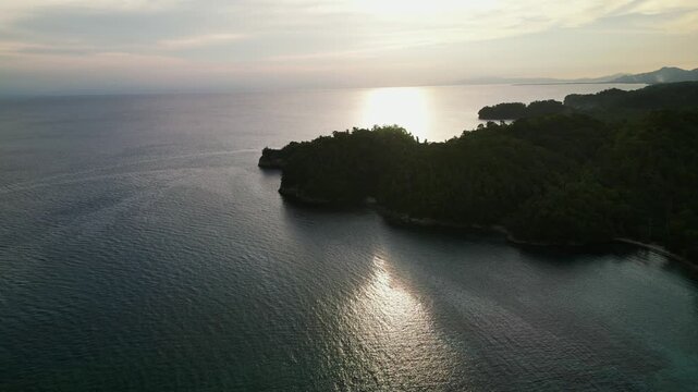 Stunning aerial dolly over the Catanduanes coastline with calm ocean, forested tropical island, and sunset light across the water