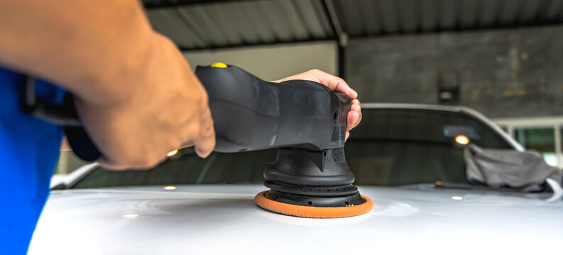 Close up auto body technician using buffer tool polishing car in body shop