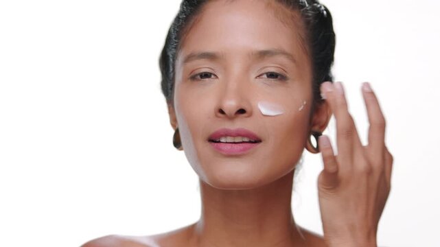 Close-up shot of south american woman light brown complexion applies cream on cheek on white background | Beauty commercial concept