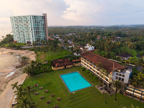 Aerial view of Gintota beach featuring a large swimming pool, a modern high-rise hotel, and lush palm trees along the coast in Galle, Southern Province, Sri Lanka.