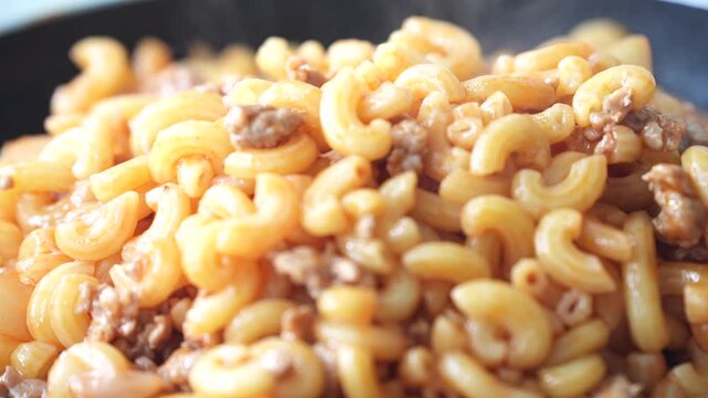 Hot macaroni stir-fried with minced meat in a pan, offering a delicious aroma and a comforting homemade meal