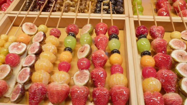 Candied fruit tanghulu skewers featuring strawberries, grapes, figs, and other sweet treats arranged in rows, offering popular street food at a lively night market in Beijing, China, Asia