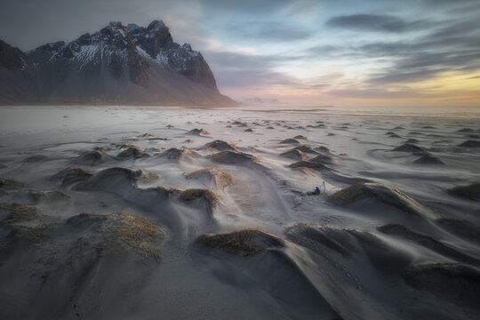 Aerial view of Stokksnes beach featuring black sand dunes and the majestic Vestrahorn mountain under a soft sunset sky with a photographer Sveitarfelagid Hornafjordur, Iceland.