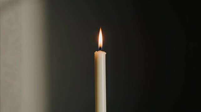 A simple candle flame flickers softly in a dark neutral room.
