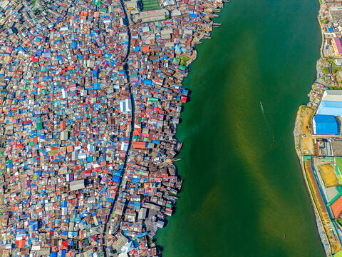 Aerial view of densely packed colorful rooftops of an informal settlement along a dark green river in Monrovia, Montserrado, Liberia.