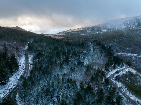 Aerial view of winding roads through snow-covered pine forests in the Serra da Estrela mountains under a misty winter sky Unhais da Serra, Castelo Branco District, Portugal.