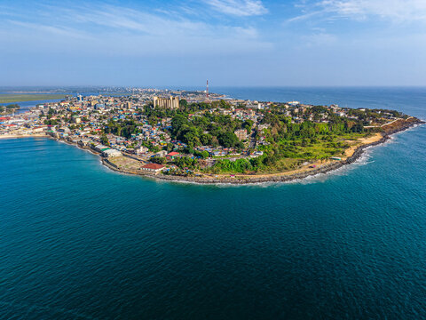 Aerial view of the coastal city featuring dense urban buildings, lush green vegetation, and a rocky coastline along the blue Atlantic Ocean Monrovia, Montserrado, Liberia.