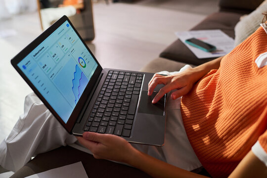 Young woman reviewing social media analytics on laptop, tracking influencer campaign performance from home. Ideal for creator marketing, brand partnerships, remote work, close up